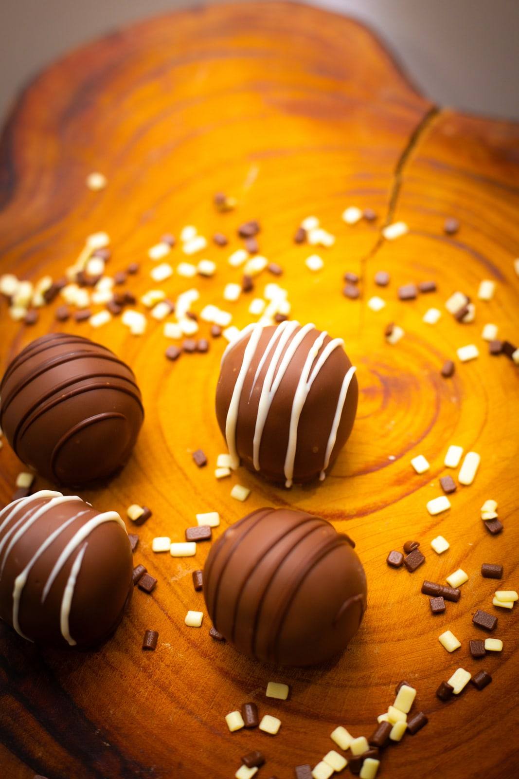 Trufas de chocolate com listras brancas sobre tábua de madeira com granulados.