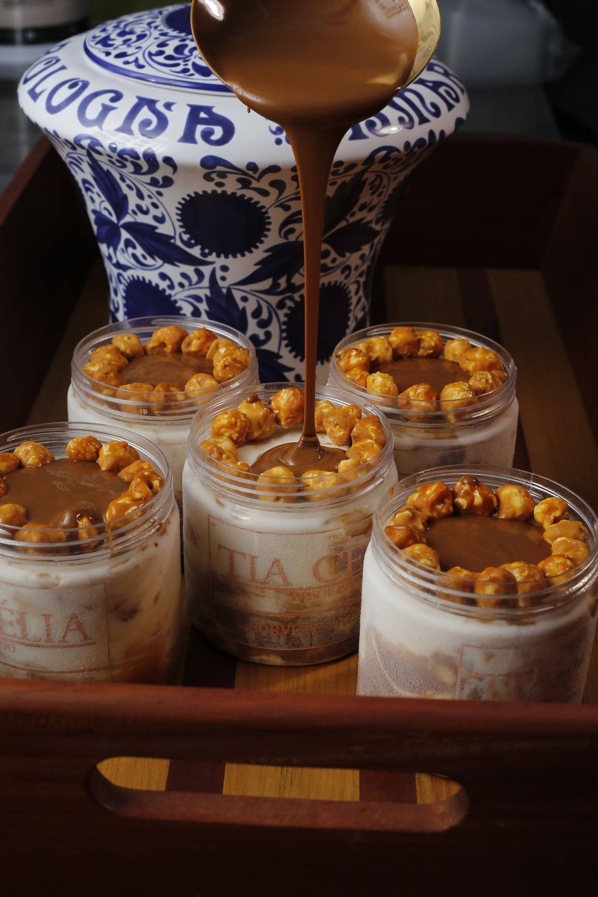 Potes de gelato Explosão de Pipoca recebendo calda de caramelo, com uma coroa de pipocas caramelizadas.