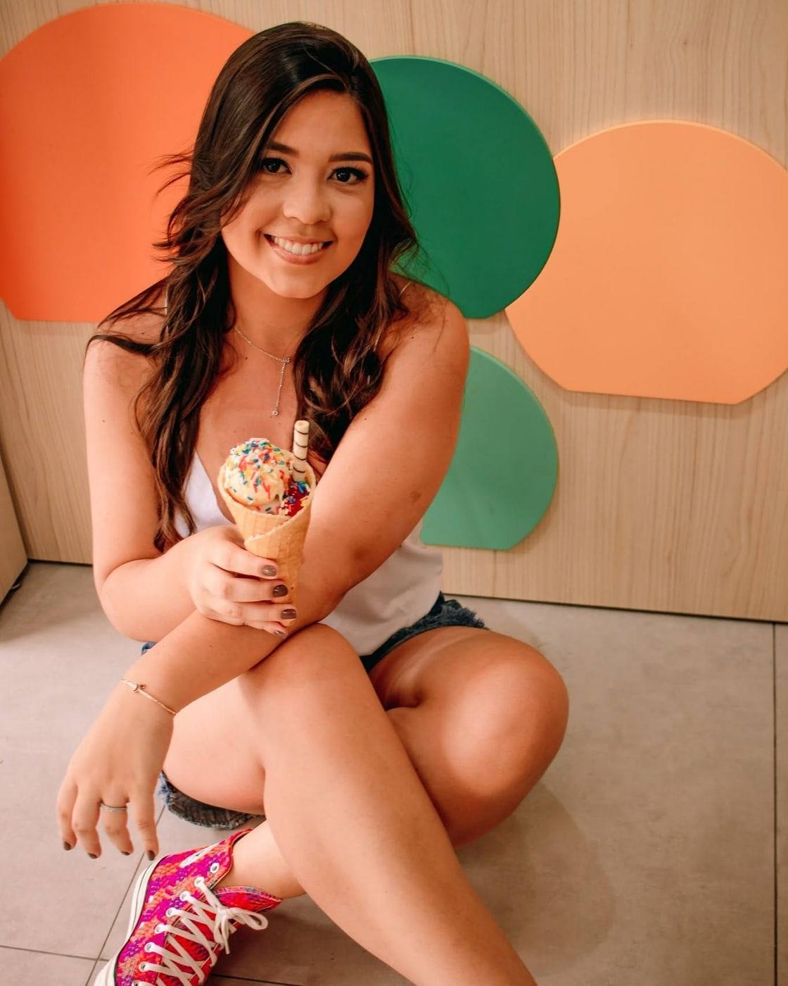 Elisa, neta da Tia Célia, sentada no chão da loja e sorrindo com um cascão de sorvete coberto de confeitos.